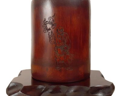 Chinese carved bamboo Zhang Zhihe poem bitong, with a finely carved Buddhist monk, Fuhu Luohan, holding a flaming ring on one side, and a famous Zhang Zhihe poem in finely carved kaishu script, about his banishment from the Imperial court, on the other side. The finish is lustrous and very fine. The brushpot has a deep, inset, natural base. The finely carved, live edge, Chinese, hongmu stand is...