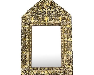 Antique French brass repose beveled mirror over board. The frame has a classic French repouss style, featuring intricate floral and scrollwork patterns and a heraldic escutcheon shield at pentacle of the frame. The design reflects Baroque and Rococo influence. The mirror shows signs of desilvering around the edges. This is common in antique mirrors exposed to moisture or age-related degradation...