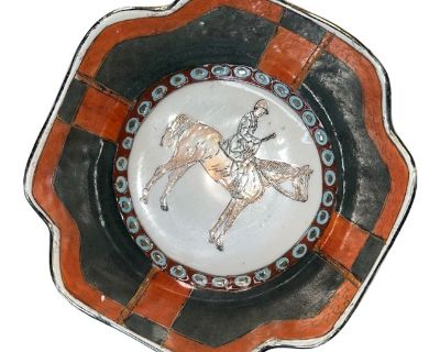 This vintage Japanese Kutani ceramic dish features a beautifully hand-painted equestrian scene at its center, showcasing a rider on horseback rendered in delicate line work. Surrounding the scene is a striking border of turquoise and white circular eye motifs, framed by bold blocks of deep charcoal and rust-orange enamel a color palette strongly associated with early 20th-century Kutani export ...