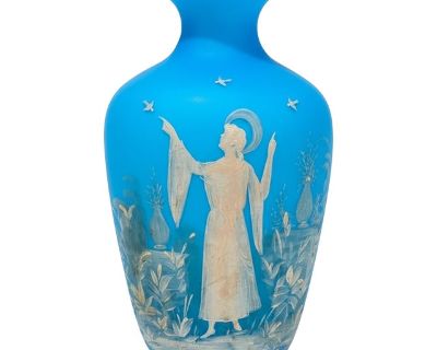 This striking antique Bohemian vase features vibrant sky blue cased glass with an opaline white interior. The surface is adorned with finely executed white enamel painting in the style characteristic of late Victorian/Edwardian Bohemian glasshouses. The central motif depicts a classical or allegorical figure in flowing robes surrounded by birds and lush foliage, with additional delicate landsca...
