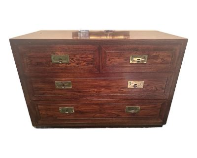 A gorgeous mid-century modern Hollywood Regency Campaign style dresser or credenza Masterfully crafted from rich wood with a natural grain finish, this chests is accented with striking brass hardware, exemplifying both form and function. Their compact yet spacious design features four drawers, offering ample storage to organize your essentials while maintaining a chic aesthetic. Adds a touch of...