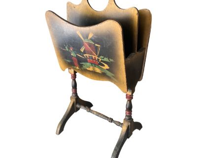 This 1920's wooden magazine rack features two charming hand-painted Dutch scenes, dual compartments for storage, and elegant turned legs. A nostalgic piece with practical functionality and timeless design. Ideal for adding a unique touch of rustic charm to your living space. Hand-painted windmill & boat designs on wood Dual compartments for organizing magazines or books Sturdy turned wooden leg...