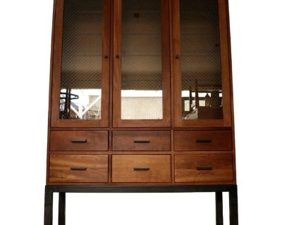 Vintage solid cherry china cabinet hutch for sale. It was manufactured here in the US by Room & Board, and is a very high-quality designer piece. It's made of solid cherry in a natural cherry finish. It has a contemporary industrial blended with Midcentury aesthetic, and is quite a nice piece to decorate. It has a metal base with clean pull handles in the same finish. The three glass cabinet do...